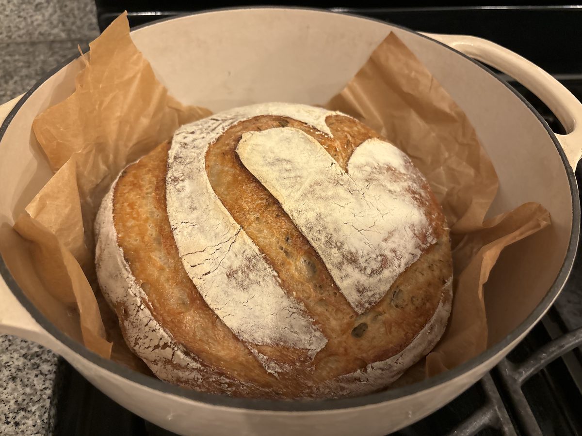 Classic sourdough boule in Dutch oven with parchment, golden flour-dusted crust